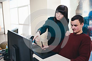 Two beautiful young office workers looking at a computer monitor and discuss the project. The situation in the office.