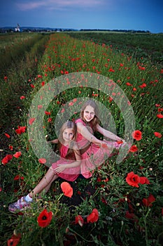 Two beautiful young sisters walking in poppy field