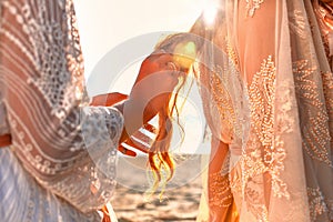 Two beautiful young woman in elegant boho dresses oudoors at sunset