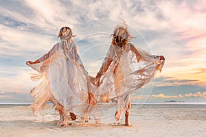 Two beautiful young woman in elegant boho dresses outdoors at sunset