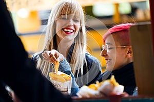 Two beautiful young women buying barbecue potatoes on a food truck in the park.