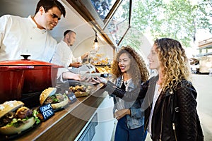 Two beautiful young women buying meatballs on a food truck.