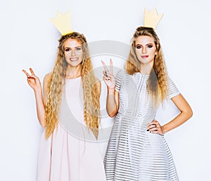 Two beautiful young women celebrate party show victory sign on white background. Best friends wearing stylish evening