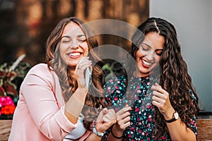 Two beautiful young women listening music with cellphone and earphones and singing while sitting outdoors