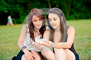 Two beautiful young women looking at smart phones outside