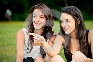 Two beautiful young women in a park pointing