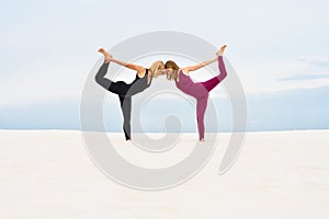 Two beautiful young women performing steamy yoga on the beach