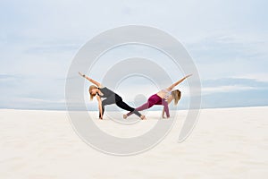 Two beautiful young women performing yoga pose parivrita parshvakonasana