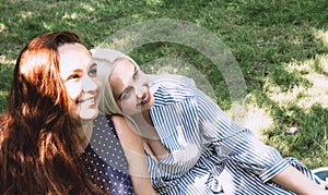 Two beautiful young women sit side by side on the grass