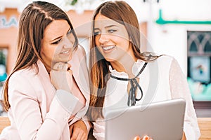 Two beautiful young women sitting on a bench and looking at the tablet