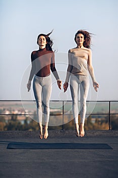 Two beautiful young women synchronously jump on the roof outdoor