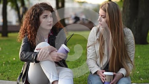 Two beautiful young women talking and drinking coffee outdoors