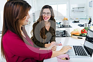 Two beautiful young women working with laptop in the kitchen.