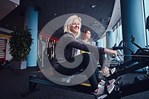 Two beautiful young women working out on rowing machines at the modern gym. Cross training