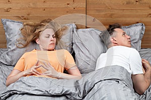 Two in bed, a woman looks thoughtfully at the man who turned away, fingering his fingers. Relationship concept