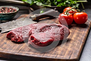 Two beef rump steaks with herbs tomatoes salt and spices on butcher board