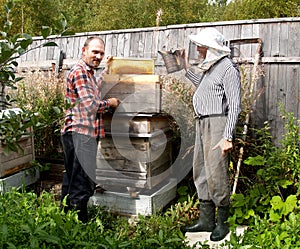 Two beekeepers work about a beehive. Summer