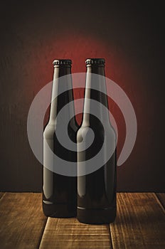 two beer bottles a dark background with red light/two beer bottles a dark background with red light. Selective focus