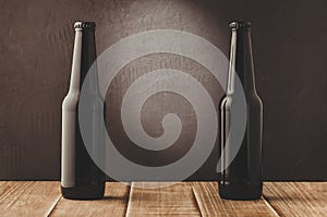 two beer bottles on a wooden table against a dark background/black bottles of beer against a dark background with this light, cop