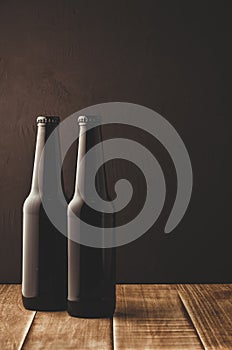 two beer bottles on a wooden table against a dark background/ two beer bottles on a wooden table against a dark background,