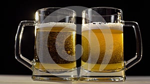 Two beer glasses are poured with foamy golden light beer on black background, beer with friend, drinks for two people