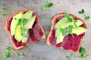 Two beet hummus and avocado toasts on a gray background