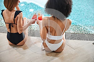 Two best friends in bikinis drinking by the pool