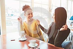 Two best friends are sitting in cafe and spending good time together. Girls are drinking some latte and enjoying their