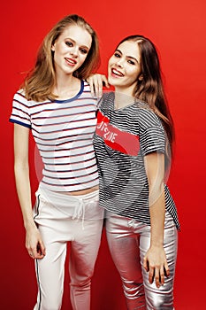 Two best friends teenage girls together having fun, posing emotional on red background, besties happy smiling, lifestyle