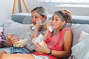 Two best friends watch sad movie at home in bed crying touching. girls hold popcorn and tv remote control looking screen romantic