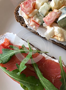 Two beterbrods with red fish and a rocket are lying on a white plate. Selectiv focus