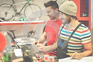 Two bicycle repairer colleagues working in bike garage - Positive mood bmx seller using computer in workshop  - Retail selling and