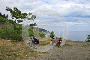 Two bicycles loaded for travel stand on the Black Sea coast, overlooking the Temple lighthouse of St. Nicholas the Wonderworker