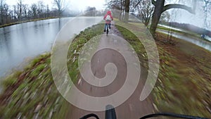 Two bicyclists ride on a muddy country road near the lake