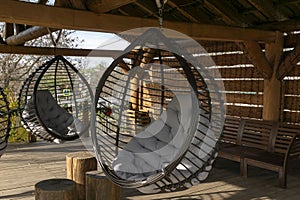 two big comfortable rotang round hanging chairs with grey pillow on outdoor wooden backyard