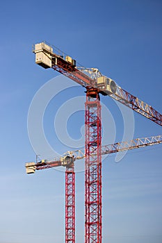 Two big jib cranes against a cloudless blue sky at the construction site of a large recreation complex in the city of