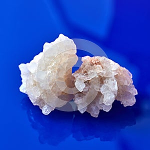 Two big peices of natural crystal of salt on a blue background with reflection.