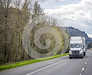 Two big rigs industrial semi trucks with semi trailers running in convoy on the wide road with mountain on the side