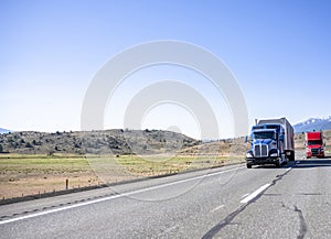 Two big rigs semi trucks red and blue colors transporting cargo in semi trailers running on the straight like arrow road