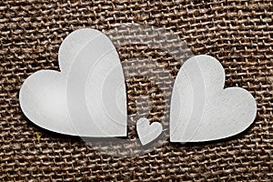 Two big silver wooden hearts and one small heart between them on brown cloth background. Symbol of two parents and one child