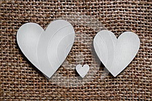 Two big silver wooden hearts and one small heart between them on brown cloth background. Symbol of two parents and one child