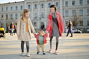 Two big sisters and their baby brother having fun outdoors. Two young girls holding their baby boy sibling on sunny spring day.