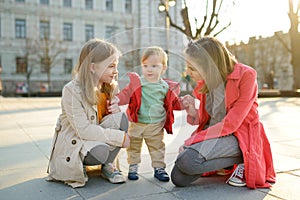 Two big sisters and their baby brother having fun outdoors. Two young girls holding their baby boy sibling on sunny spring day.