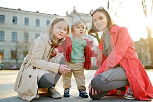 Two big sisters and their baby brother having fun outdoors. Two young girls holding their baby boy sibling on sunny spring day.