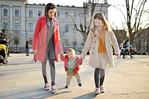 Two big sisters and their baby brother having fun outdoors. Two young girls holding their baby boy sibling on sunny spring day.