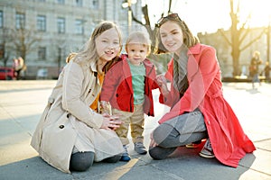 Two big sisters and their baby brother having fun outdoors. Two young girls holding their baby boy sibling on sunny spring day.