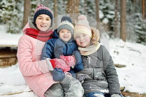 Two big sisters and their baby brother having fun outdoors. Two young girls holding their baby boy sibling on winter day. Kids