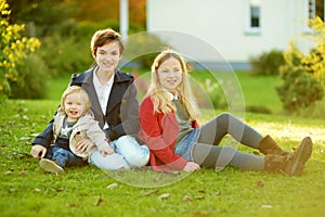 Two big sisters and their little brother having fun outdoors. Two young girls holding toddler boy on autumn day. Children with