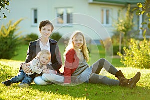 Two big sisters and their little brother having fun outdoors. Two young girls holding toddler boy on autumn day. Children with