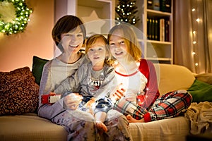 Two big sisters and their toddler brother playing with Chistmas lights in a cozy living room on Christmas eve. Kids spending time